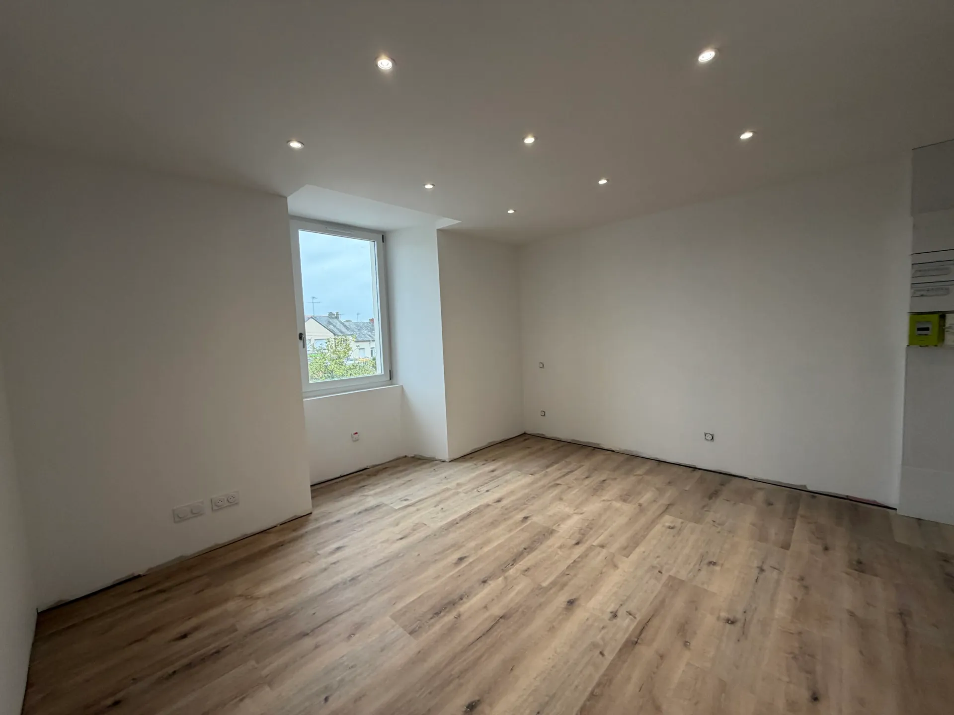 Pièce lumineuse d’un logement rénové par Vestae, spots encastrés et parquet stratifié